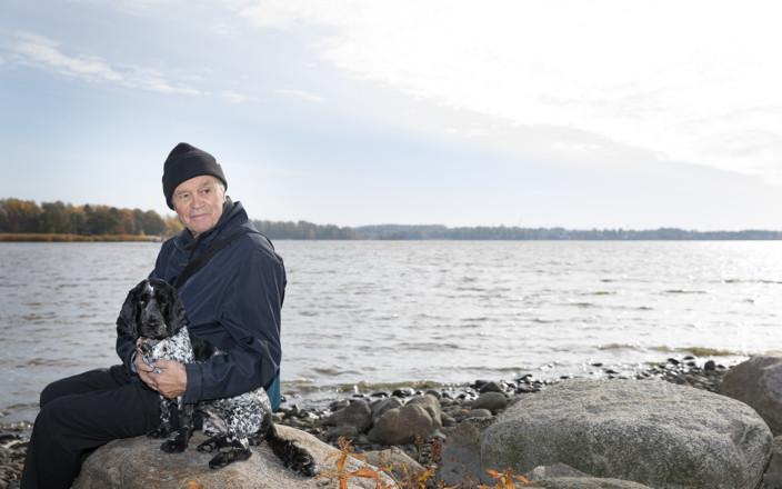 Neurologian professori Juhani Wickström koiransa kanssa rantakivellä
