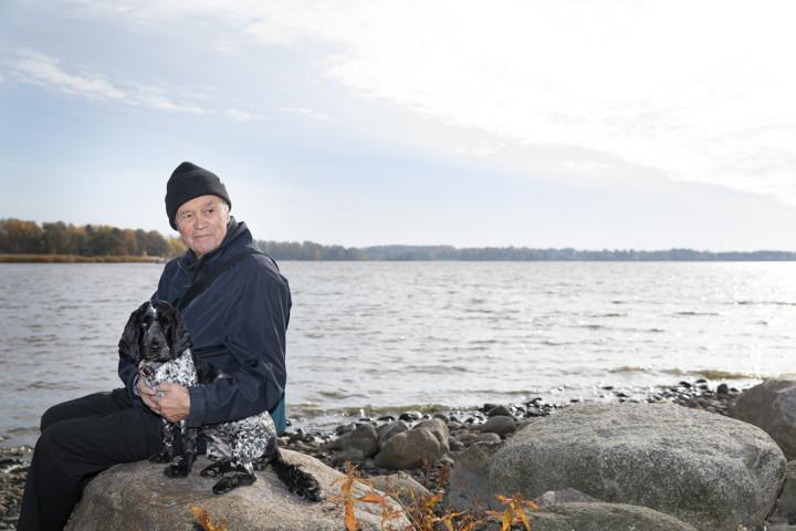 Neurologian professori Juhani Wickström koiransa kanssa rantakivellä