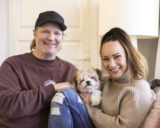 Kim ja Mari Sainio istuvat kotisohvallaan koiransa kanssa