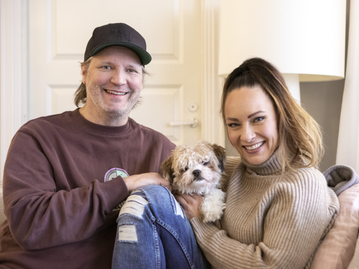 Kim ja Mari Sainio istuvat kotisohvallaan koiransa kanssa