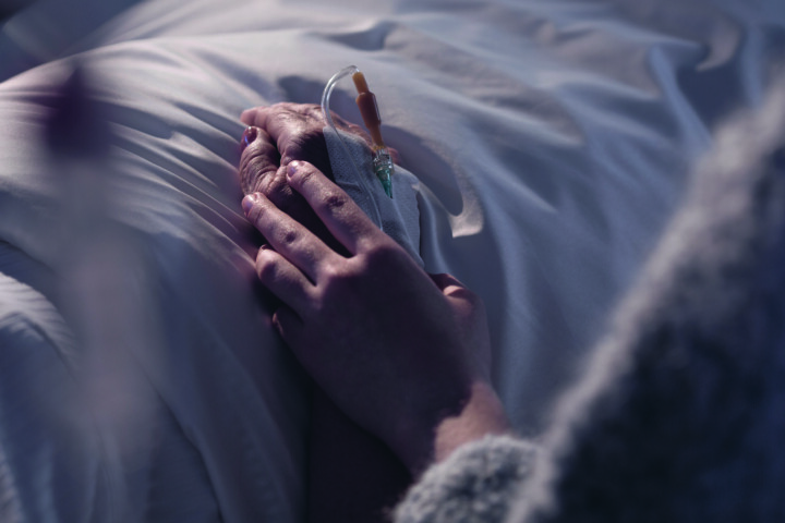 Läheinen ihminen pitää sairaalavuoteessa makaavaa potilasta kädestä.