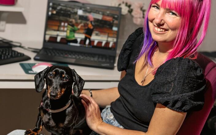 Sara Kaasalainen istuu työpöydän ääressä, sylissään mäyträkoira ja hymyilee kameralle